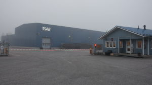 Fabriken i Lappvik. En fabrik i dimmigt septemberväder. Framför byggnaden en röd-vit bom och ett rött trafikljus.