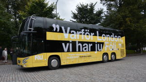 Dubbeldäckaren är solgul som de andra Fölibussarna. Dubbeldäckarbussen är gul och över hela sidan står frasen "Varför London, vi har ju Föli".