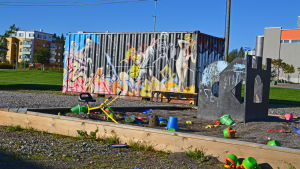 Leksaker för småbarn och konst för vuxna Sandlådan vid containern med profesionell graffiti