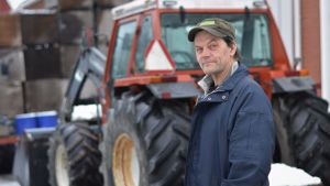 Christer Finne hemma på gården i Solf. Nu har det gått tio år sedan sonen Erik dog och hallen brann ner. Man i keps står framför en traktor och ser in i kameran.