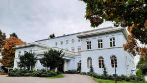 Haiko Gård välkomnar gäster som vanligt. En ljusblå och vit herrgårdsbyggnad. Framför syns träd med orange höstlöv.