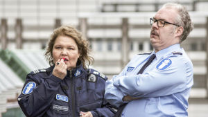 Rauni (Kaarina Hazard) och Jarkko Larsson (Mikko Roiha) funderar hur de skall lösa det hela. Rauni Kolehmainen (Kaarina Hazard) och Jarkko Larsson (Mikko Roihaä) står bredvid varandra i polisuniform.