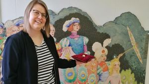 Museiguiden Katarina Forslund framför en del av Alexander Reichsteins installation "I slottet". I bakgrunden Rudolf Koivus pärm till den finska versionen av Adalminas pärla, WSOY 1957. Museiguiden Katarina Forslund framför en del av Alexander Reichsteins installation "I slottet". Rudolf Koivus pärm till den finska versionen av Adalminas pärla, WSOY 1957. Topelius sagoland. Nykarleby 2018.