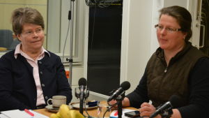Soile Gustafsson och Rannvi Wallen. Två Ingåpolitiker sitter vid ett bord i en radiostudio. En mikrofon, frukt, papper och pennor på bordet.