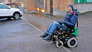 Jonas ute på gatan, försöker ta sig upp på en trottoarkant med rullstolen. 