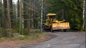 Vissa avsnitt av Skogbyvägen är väldigt smala. Ett gult fordon som jobbar med att jämna ut en grusväg.