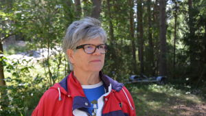 Elisabeth Nymalm, ordförande för byarådet. Närbild på Elisabet Nymalm. Hon står i skogsbrynet, har grått hår och glasögon.