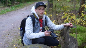 Joachim Munther spanar efter ekorrar att fotografera. Person med kamera på huk vid sten och grusväg.