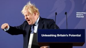 Storbritanniens premiärminister Boris Johnson vill möblera om i sin regering efter jordskredssegern i parlamentsvalet december. Boris Johnson står vid ett podium och håller tal. Han tittar neråt, viftar med handen och skriker.