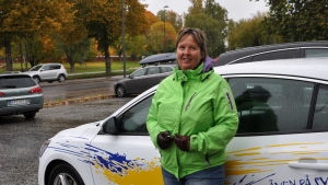 Ulla Nummelin jobbade tidigare som taxichaufför, numera är hon trafiklärare. Ulla står vid trafikskolans vita bild som har reklamtejpning på utsidan.
