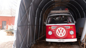 Kleinbussen Kuukkeli har tagit sina ägare på många äventyr, och kommer nu att fungera som tak över huvudet i väntan på hustak av olika slag. En rödvit glänsande Wolkswagen-bil står parkerad i ett grått biltält.