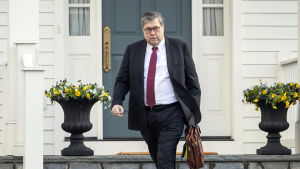 USA:s justitieminister William Barr William Barr, i röd slips, lämnar sitt hem med en tunn läderportfölj i handen.