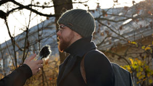 Miro Rein tycker att det på grund av de små kretsarna finns en gemenskapskänsla bland finlandssvenskar som inte finns bland den finskspråkiga befolkningen. En man står med sidan mot kameran. En hand från vänster håller en bandspelare i höjd med mannens mun.