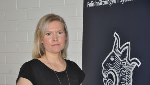 Sara Malm. Ädre kriminalkonstapel Sara Malm står vid en banderoll med polisens lejonemblem.