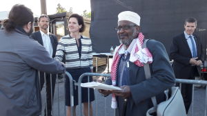 Mohamed Hagi Farah hoppas att 82 önskemål från föräldrar i Järva, inte ska glömmas bort efter politikerveckan. I bakgrunden Moderaternas partiledare Anna Kinberg Batra. Mohamed Hagi Farah ser glad och nöjd ut, står med en lista i handen, Anna Kinberg Batra i bakgrunden