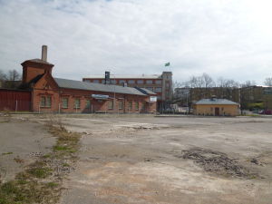 Sprucken asfalt på paradplats i Ekenäs. I bakgrunden syns stadshuset med Raseborgsflaggan. Sprucken asfaltplan med byggnader i bakgrunden.