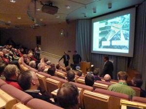 Auditoriet var fullsatt. Längst framme från vänster planläggningskonsulten Anssi Savisalo, stadsplaneringsarkitekten Simon Store och tekniska direktören Jan Gröndahl. Publik i auditorium tittar på bilder som visas om en plan för Norra hamnen i Ekenäs.
