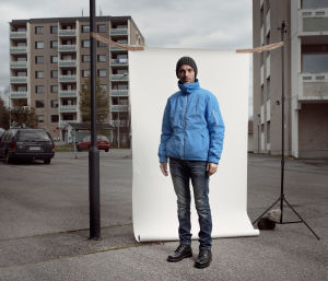 Irakilainen turvapaikanhakija, Maytham, seisoo valkokankaan edessä parkkipaikalla.