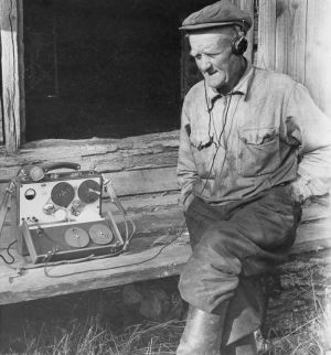 Maanviljelijä Otto Ritari riihen ovella maatilallaan Valkealassa vuonna 1958. Radiotyö. Kaarle Nordenstrengin radio-ohjelma Ritarin talosta. Maanviljelijä Otto Ritari kuuntelee kuulokkeilla nauhoituksen tulosta riihen ovella maatilallaan. Maihak- äänityslaite, maihakki. Yleisradion ohjelmat.