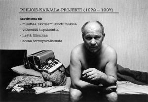 Mies istuu sängyllä ja katsoo kameraan