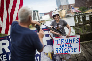En kvinna som stöder Trump poserar med hjälm, gevär tillsammans och skylten "Trumps murbrigad".
