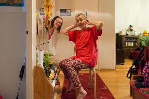 Aili on ollut alusta alkaen sitä mieltä, että jos tämä yhteisen matkamme kuvaus voi auttaa jotakuta — lohduttaa tai lieventää synkkiä ajatuksia diagnoosin saamisen jälkeen — on se kaiken vaivan arvoista. tytär kurkistaa ovesta, äiti etualalla laittaa papiljotteja