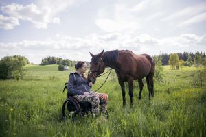 Nicole Hellberg sitter i sin rullstol ute i hagen med sin häst.