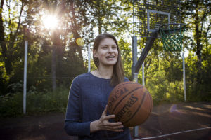 Ung kvinna med blå tröja i närbild. Hon håller i en basketboll.