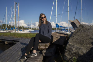 Sara Jakobsén sitter på en brygga. Hon har blå tröja och svarta byxor. I bakgrunden syns segelbåtar.