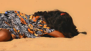 Tyttö makaa aavikolla hiekassa.