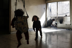 Två barn leker medan deras pappa försöker tända eld på några bitar papper för att värma mat. FN larmar om kris i Ghouta.