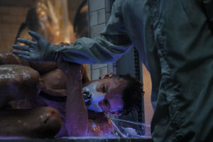Altered Carbon on Netflixin jättisatsaus. Sikiöasennossa oleva limainen mies tarrautuu suojapuvussa olevan henkilön käteen.