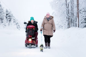 Katri Blomqvist kävelee Mano-koiran kanssa ja Erno Blomqvist ajaa vieressä sähkömopolla.