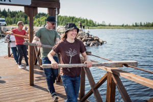 Upptäcktsresan till ön Varjakansaari får sin början vid fastlandet, säger Tanja Råman: Tanja Råman, Rasmus Tåg ja Nicke Aldén vetävät kapulalossin kapuloilla vaijeria taaksepäin, ylitetään salmea Varjakassa Oulussa.