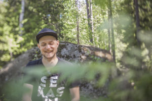 Mikko Toiviainen luonnossa, istuu ison kiven edessä.