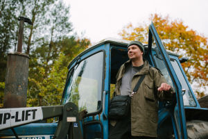 Juha Rasimus seisoo traktorin oven edessä.