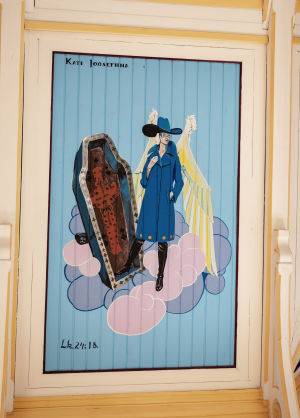 Enkeli pukeutuneena sinisävyisiin muodikkaisiin takkiin ja saappaisiin, taulun yläosassa teksti Kati Josefiina.