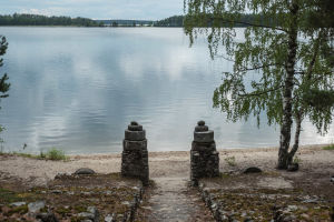 Kaksi kivitolppaa, taustalla hiekkaranta ja järvi.
