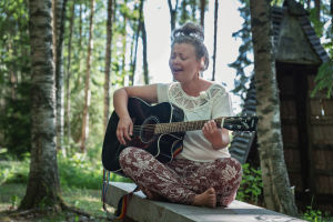 Muusikko Heidi Niinimäki soittaa kitaraa Alpo Jaakolan patsaspuistossa, ympärillä vihreää metsää.