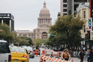 En del av staden Austin i Texas fotograferad i gatunivå. I bakgrunden en stor byggnad med pelare, kupoler och spira.