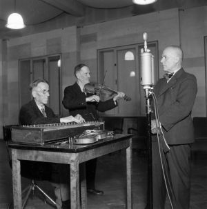 A. O. Väisäsen vieraina studiossa kanteleensoittaja Matti Koskinen ja viulisti Tapio Savioja vuonna 1944. A. O. Väisänen radion studiossa mikrofonin ääressä. Vas.Matti Koskinen soittaa kanteletta ja Tapio Savioja viulua,