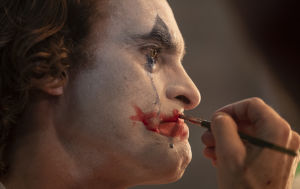Närbild då Arthur (Joaquin Phoenix) sminkar sig till clown samtidigt som han gråter och blå mascara rinner nerför kinden.