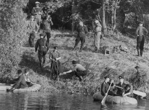 En bild från 1961 där östtyska militärer letar efter en rymling. En svartvit bild från 1960-talet med uniformsklädd män på en strandbank och i vattnet i två gummibåtsliknande farkoster sitter totalt fyra män och paddlar i väg från stranden.