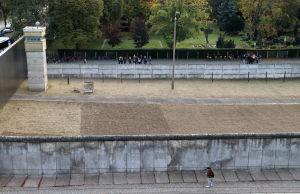 Burkhart Veigel bor bara ett stenkast från Bernauer Strasse där några av de sista delarna av Berlinmuren står kvar som minnesmärke. En bred stenmur fotograferad uppifrån. På bägge sidor finns människor som tittar på muren.