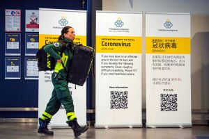 Sjukvårdspersonal på Arlanda flygplats i Stockholm. En kvinna i sjukvårdaruniform går förbi coronavirusskyltar.