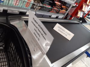 Ge varandra utrymme att plocka upp varor En skylt på rullbandet i livsmedelsaffär med uppmaningen att en kund i taget placerar sina uppköp på bandet.
