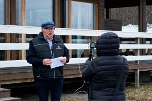 Peter Remahl håller hälsningstal till klubbmedlemmarna via livestream. En man med keps och täckjacka pratar medan en annan person filmar honom.