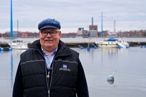 Peter Remahl. En man i keps ler mot kameran. I bakgrunden bryggor och förtöjda båtar.