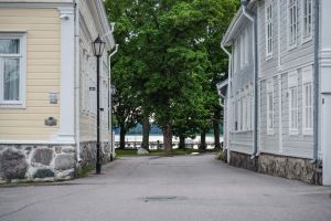 Katunäkymä, reunustoilla vanhat puutalot, kadun päässä lehtipuita ja ranta