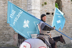 Riddare i rustning rider genom Visby med flaggor med texten "Håll avstånd" på. 